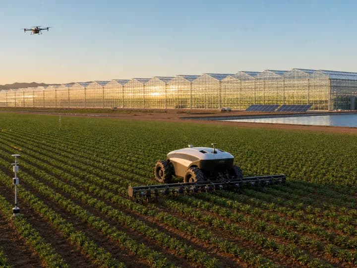 Autonomous precision tractor, field sensors and mapping drone working beside an enormous commercial multi-span glasshouse
