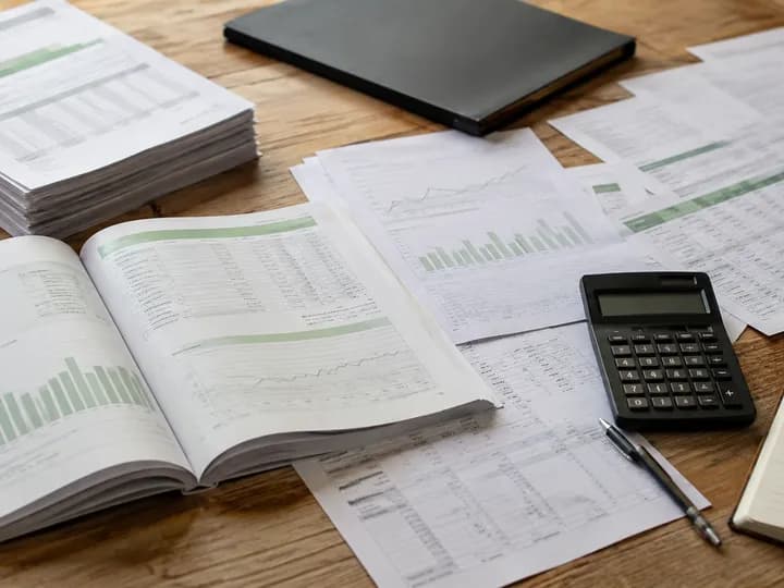 Financial reports, spreadsheets, budget charts and a calculator laid out on a desk for greenhouse project cost planning